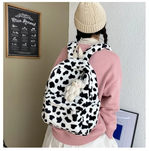 Vista dettagliata dello zaino di peluche con motivo mucca bianco e nero e ciondolo