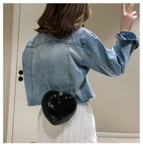 Detail of a chic black heart-shaped crossbody bag with a shiny finish and gold chain