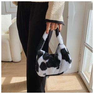 Sac à main chic en peluche à motif vache noir et blanc tenu par un mannequin élégant