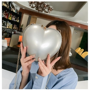 Detailed view of silver heart-shaped clutch bag with golden chain and clasp in a party setting