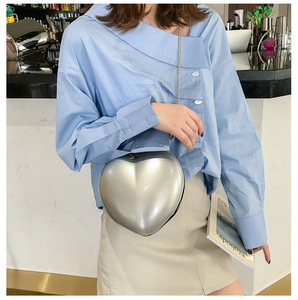 Silver heart-shaped hard shell crossbody bag with gold chain strap shown on model
