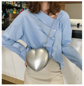 Detailed view of silver heart-shaped crossbody bag with gold chain strap worn by a model