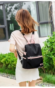 Outdoor back view of stylish black and pink color-block backpack worn by a woman