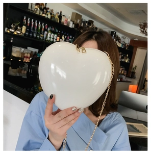 Detail of white heart-shaped crossbody bag with gold metal chain and dual zippers