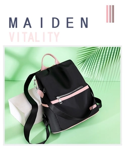 Detail of black nylon backpack with pink accents and silver metal zippers on green background