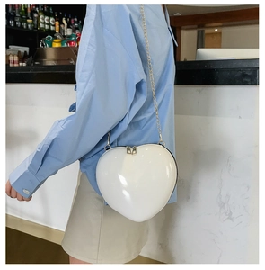 Detail showing white heart-shaped crossbody bag with gold chain strap on a model