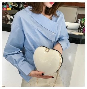 Detail of white heart-shaped chain bag with glossy finish and gold metal zipper