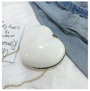 Detail of a chic white heart-shaped chain bag with glossy finish on denim background