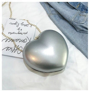 Detail of silver heart-shaped hard shell crossbody bag with a delicate gold chain strap