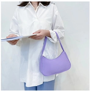 Detail of a purple nylon croissant shoulder bag with zipper closure shown on a model