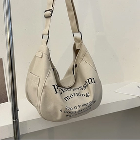 Dettaglio della borsa a mezzaluna in tela beige con stampa di lettere nere e tracolla
