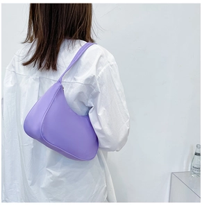 Close-up of a minimalist purple nylon hobo bag worn by a model against a white wall