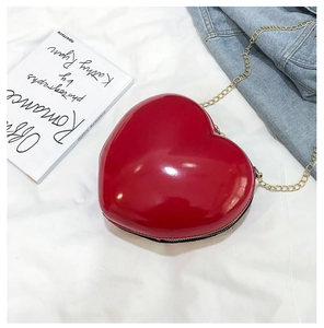 Detail of red heart-shaped evening clutch bag with gold chain on white fabric background
