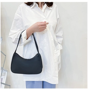 Close-up of a black nylon hobo bag worn by a model in a white shirt and blue pants