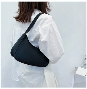 Detail view of the black nylon crescent underarm bag worn by a model against white wall