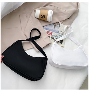 Modern black and white nylon crescent underarm bags displayed on a cozy white bed