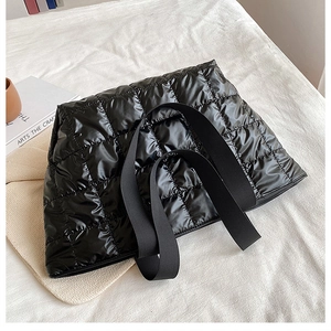 Detail shot of black quilted puffer tote bag on bed highlighting the padded nylon texture