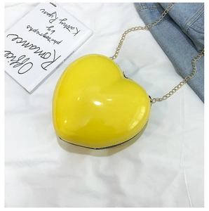 Detail of a bright yellow heart-shaped mini bag in glossy patent leather with gold chain
