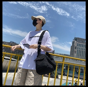 Outdoor lifestyle shot of a black canvas messenger bag with wide adjustable shoulder strap