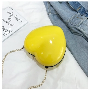 Detail view of bright yellow heart shaped chain bag with gloss finish on denim background