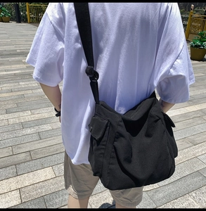 Rear view of a black canvas messenger bag featuring wide straps and side flap pockets