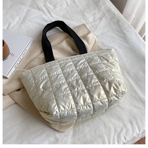 Detailed view of silver quilted down tote bag with black straps on a white background