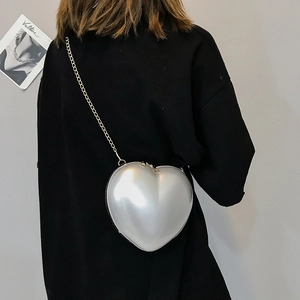 Detail of silver heart-shaped hard shell crossbody bag with elegant golden chain strap