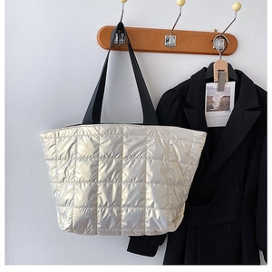 Close-up of quilted silver padded tote bag with wide black shoulder straps hanging on a wall