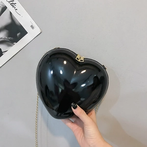 Close-up of heart-shaped black patent leather bag with gold chain and dual zippers