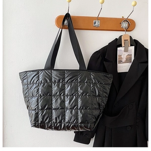 Close-up of black quilted down tote bag hanging on a wooden hanger against a white wall