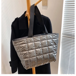 Detailed view of silver metallic quilted tote bag with black straps hanging in real setting