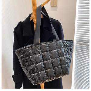 Detail of black quilted puffer tote bag in glossy nylon hanging on a wooden rack