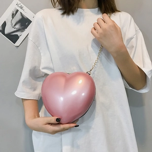Detailed view of pink heart-shaped mini clutch bag with gold chain strap on a white dress