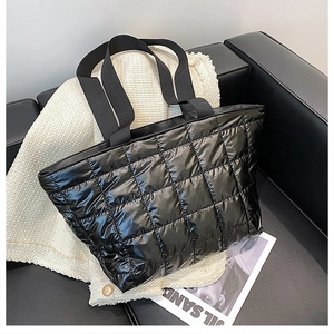 Detail of a black quilted puffer tote bag with glossy finish and wide textile handles