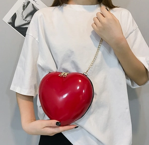 Detail of red heart-shaped patent leather crossbody bag with golden chain strap