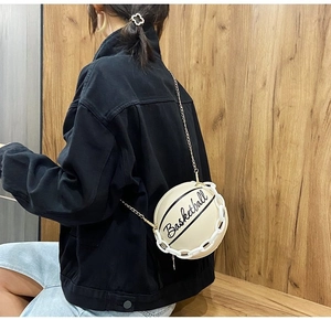 Style shot of a cream basketball-shaped crossbody bag with gold chain strap on a model