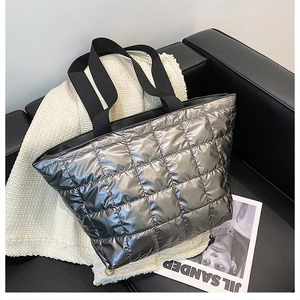 Close-up of shiny silver quilted tote bag with metallic finish on black leather sofa