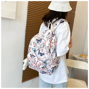 Close-up of white canvas backpack featuring colorful butterfly prints and plush pompom charm