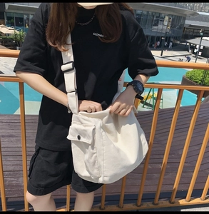 Detail of cream canvas messenger bag featuring a black adjustable strap and front pocket