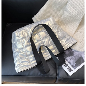 Macro detail of silver quilted down tote bag with metallic finish and wide black strap
