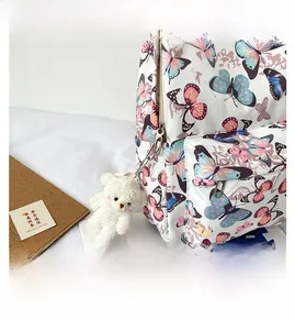 Detail of colorful butterfly print backpack with a cute plush bear charm on the side