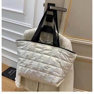 Detailed view of silver quilted down tote bag hanging next to a tweed jacket in a room