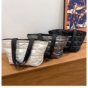 Close-up of quilted down puffer tote bags in white, silver, and black on a wooden desk