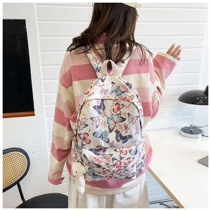 Detailed back view of a white butterfly print backpack with a cute plush bear pendant