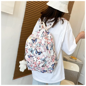 Detailed view of white canvas backpack with colorful butterfly print and bear charm