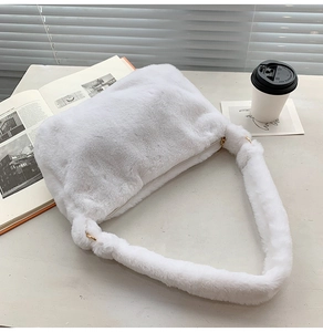 Nahaufnahme der weichen weißen Plüschtasche mit Goldringen auf minimalistischem Tisch