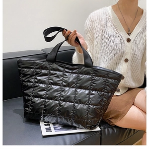Close-up of black quilted puffer tote bag held by a model in a minimalist lifestyle setting