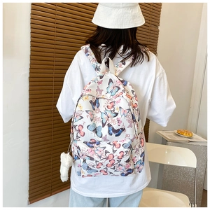 Close-up of butterfly print backpack with a white plush ball charm on side pocket