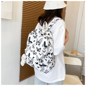 Back view of a white canvas backpack with black butterfly print worn by a person