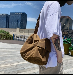Outdoor street view of a brown canvas messenger bag with flap closure and adjustable strap